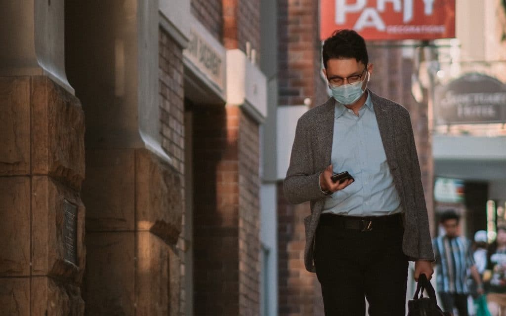 A man in a face mask uses their phone (Image by Kate Trifo)